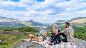 Un couple est assis sur une couverture, devant un pique-nique, et profite de la vue sur une vallée pittoresque.