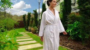 Une personne vêtue d’une robe blanche marchant sur un sentier de pierre dans un jardin bien entretenu, avec un bâtiment en arrière-plan.