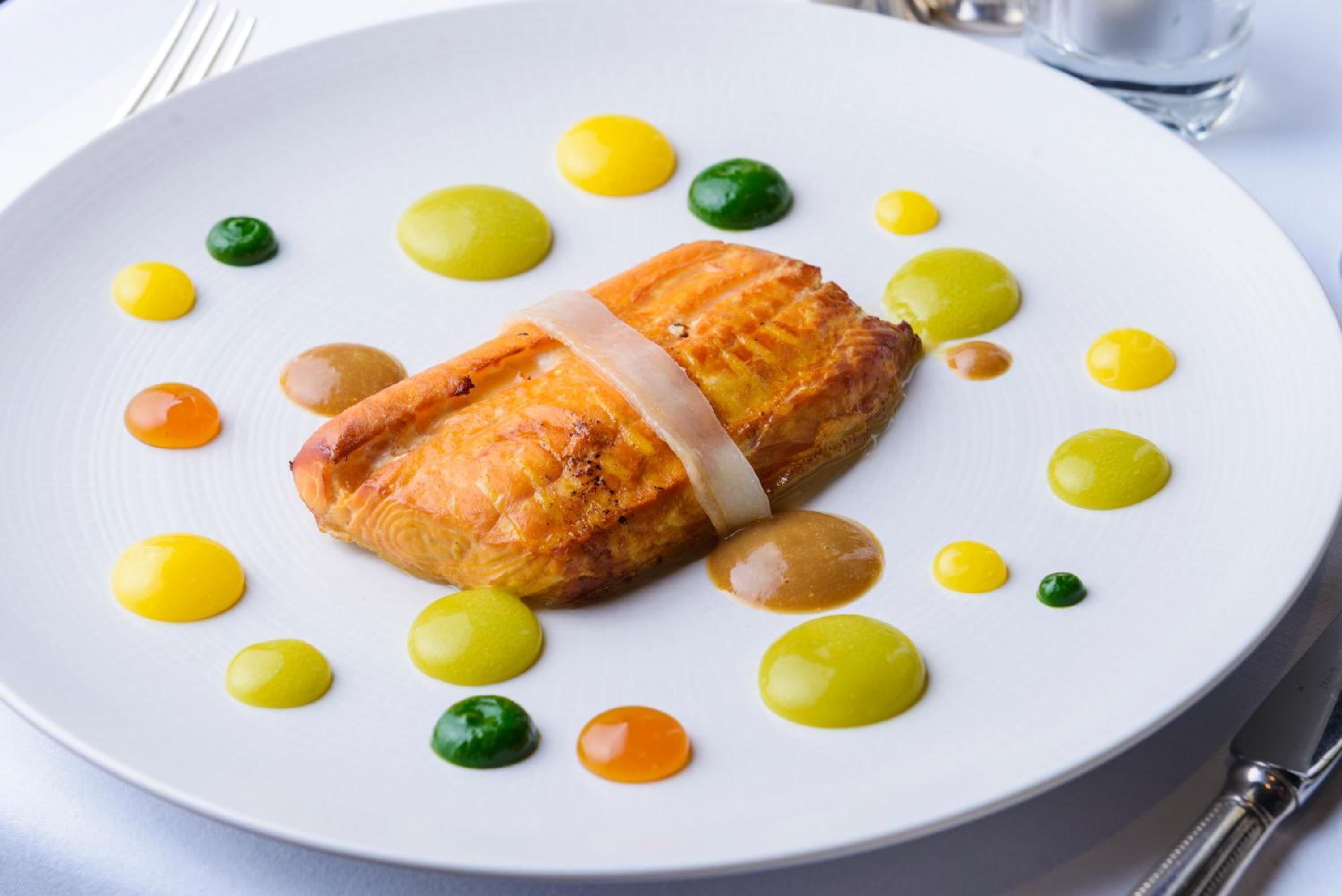 A plate with a piece of salmon, surrounded by yellow and green sauces.
