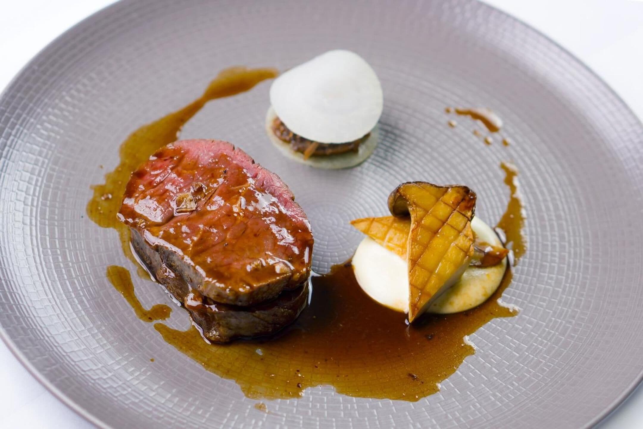 A plate with a steak, a pat of butter, and a piece of grilled fruit.