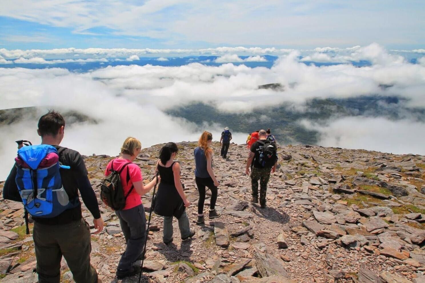 A group of hikers on a rocky mountain trail with a view of clouds below.