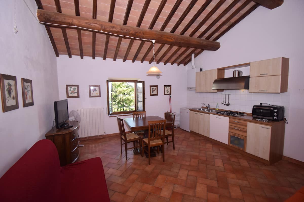 A compact kitchen with a dining table, chairs, a TV, and a red sofa.