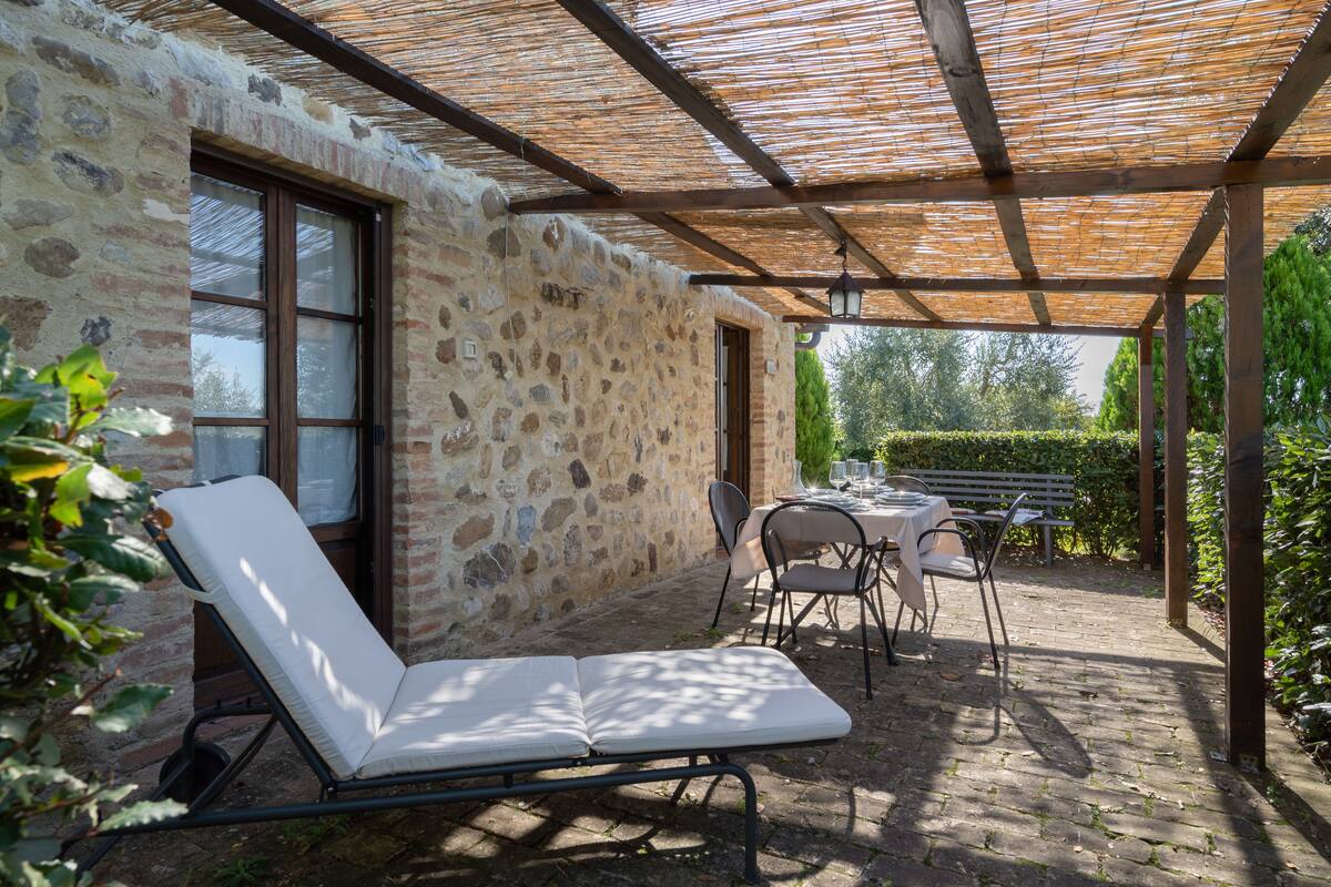 A stone building with a covered patio, a lounge chair, and a table set for dining.