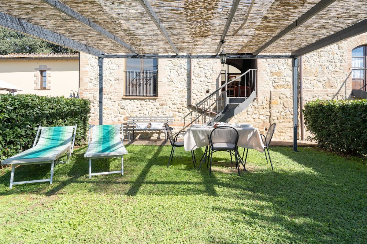 A covered outdoor patio with a stone wall, a table with chairs, and two lounge chairs.