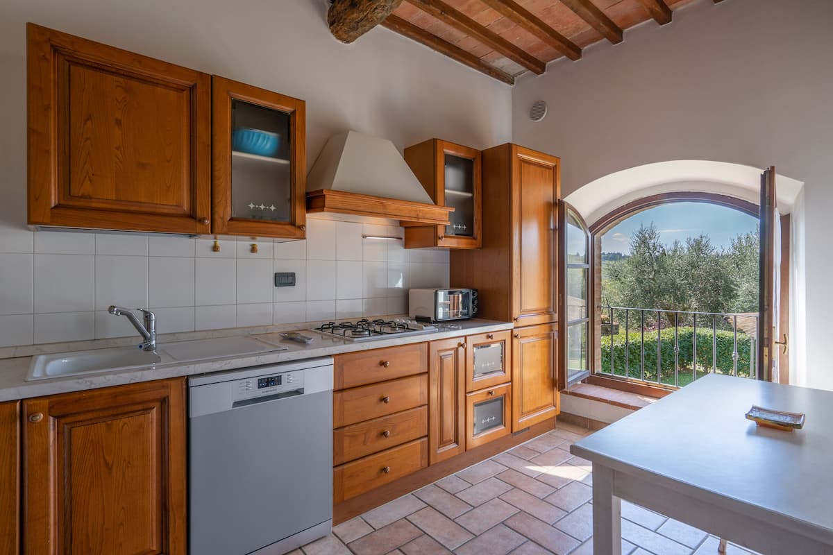A kitchen with wooden cabinets, a dishwasher, a stove, and a window overlooking a garden.
