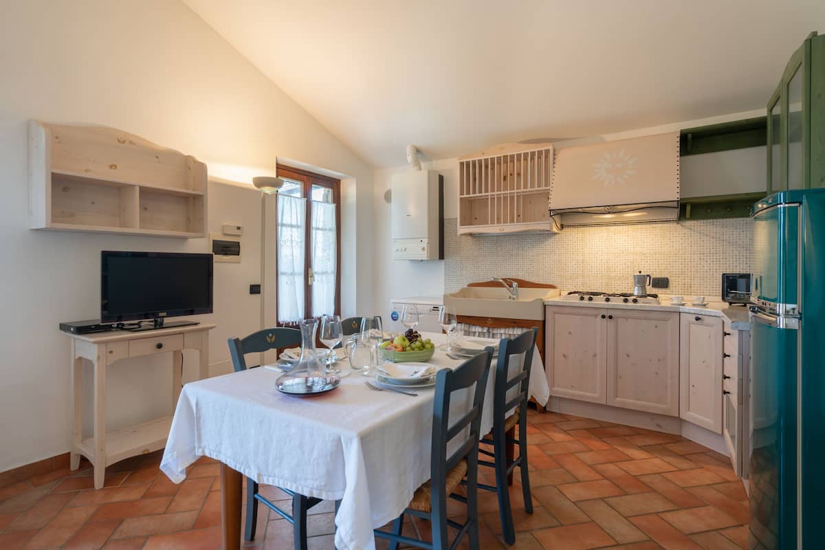 A compact kitchen with white cabinets, a dining table set for four, a television, and a tiled backsplash.