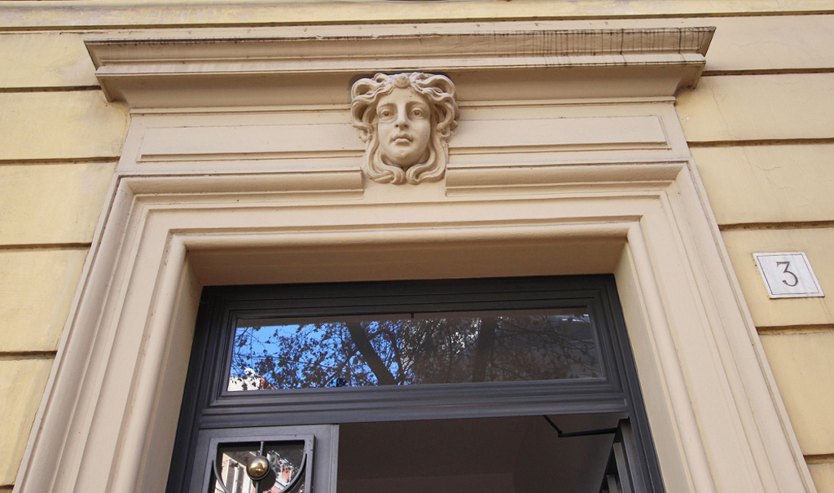 Une entrée d’immeuble ornée d’un bas-relief en pierre au-dessus de la porte et d’un chiffre « 3 » sur le mur.