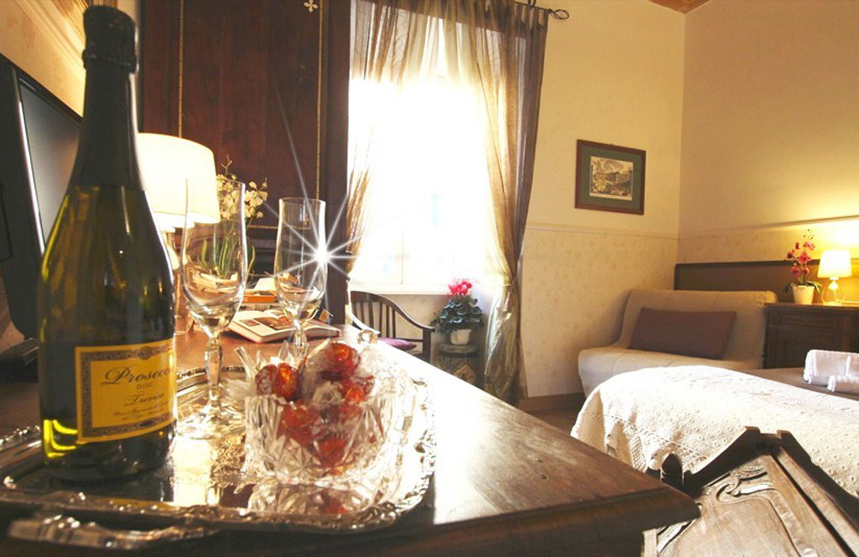 A hotel room with a dining table set with a bottle of wine, glasses, and a decorative glass bowl.