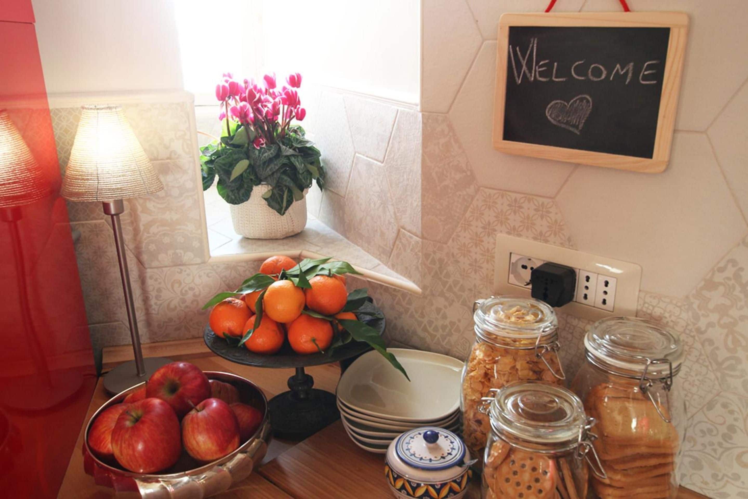 Une table préparée pour le petit-déjeuner avec des pommes, des oranges et un panneau d’accueil.