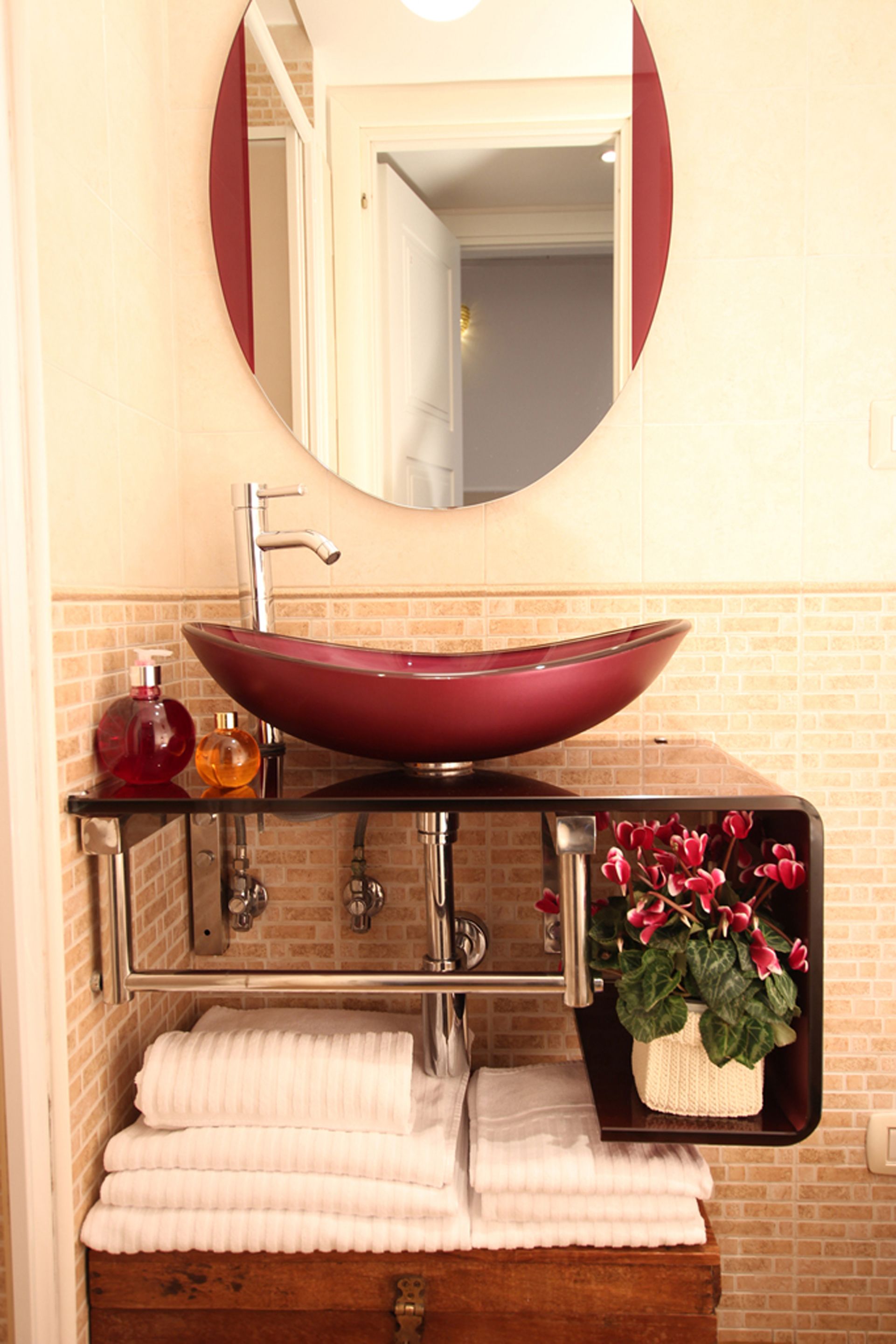 Un baño con un lavamanos tipo recipiente rojo, un espejo, un perchero para toallas y una planta en maceta.