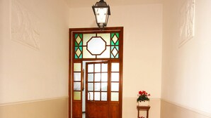 A hallway with a patterned floor, a wooden door with glass panels, and a small table with flowers. - Campanella3 (Rome)