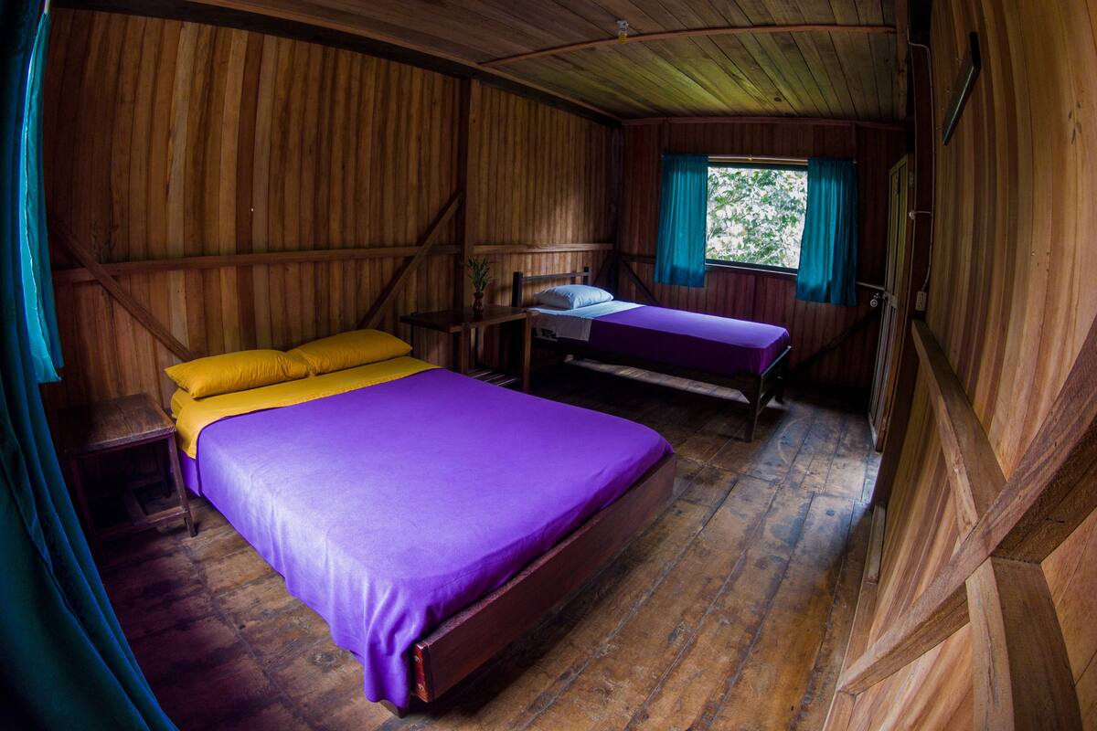 A wooden cabin room with two beds, one with yellow and one with purple bedding.
