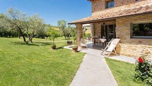 Una casa de piedra con techo de tejas, un patio con mobiliario exterior y un césped bien cuidado.