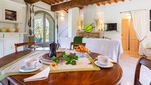 Un comedor con una mesa de madera dispuesta para el desayuno, incluyendo una cafetera, tetera y pasteles.
