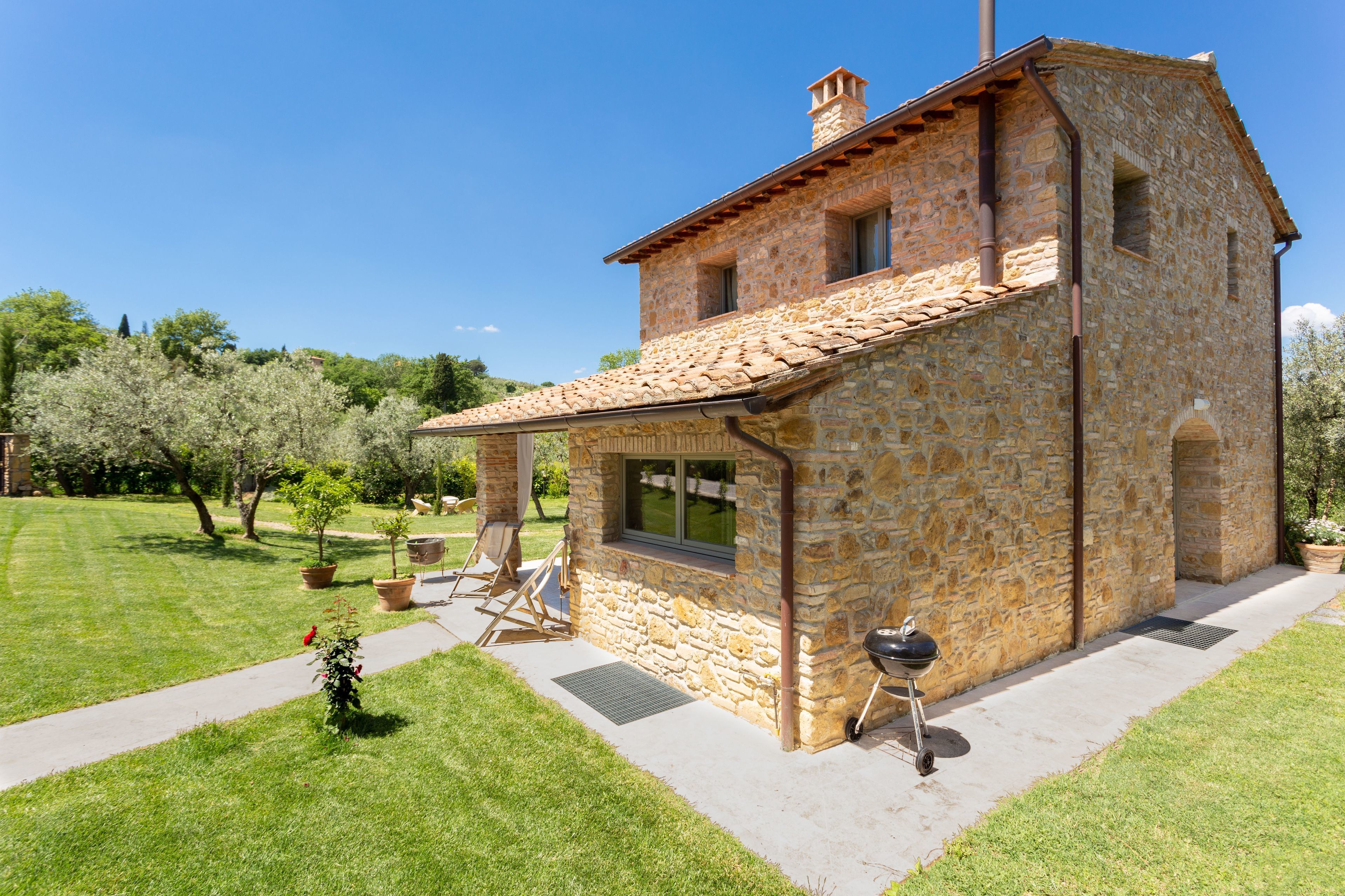 A stone house with a tiled roof, a window, and a barbecue grill outside.
