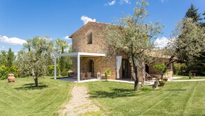 Una casa de piedra con un porche cubierto, rodeada de césped cuidado y árboles.