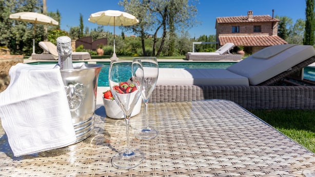 Escena junto a la piscina con una botella de champán, dos copas y un bol de fresas.