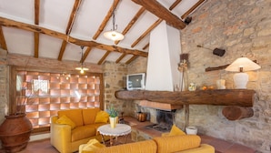 Ein rustikaler Innenraum mit Steinwand, Holzbalken, Kamin und gelben Sofas.