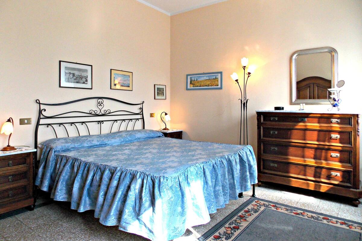 A bedroom with a bed, dresser, nightstands, and wall-mounted lamps.