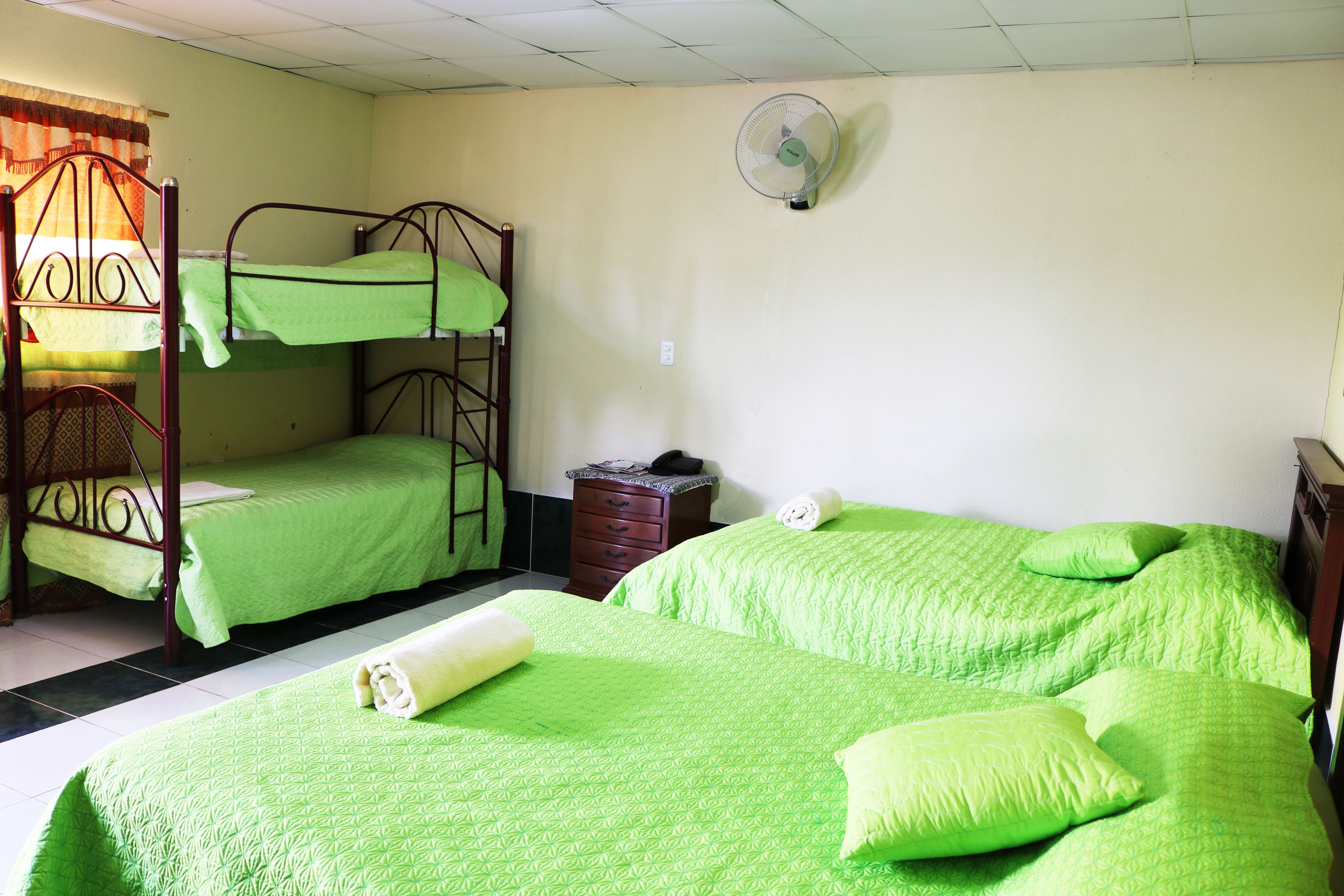 Un dormitorio con literas, una mesita de noche, un ventilador y una ventana con cortinas.