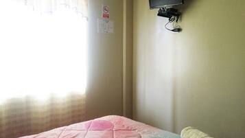 A room with a bed, a television mounted on the wall, and a window with curtains.