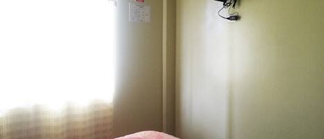 Une chambre avec un lit, un téléviseur fixé au mur et une fenêtre avec des rideaux.
