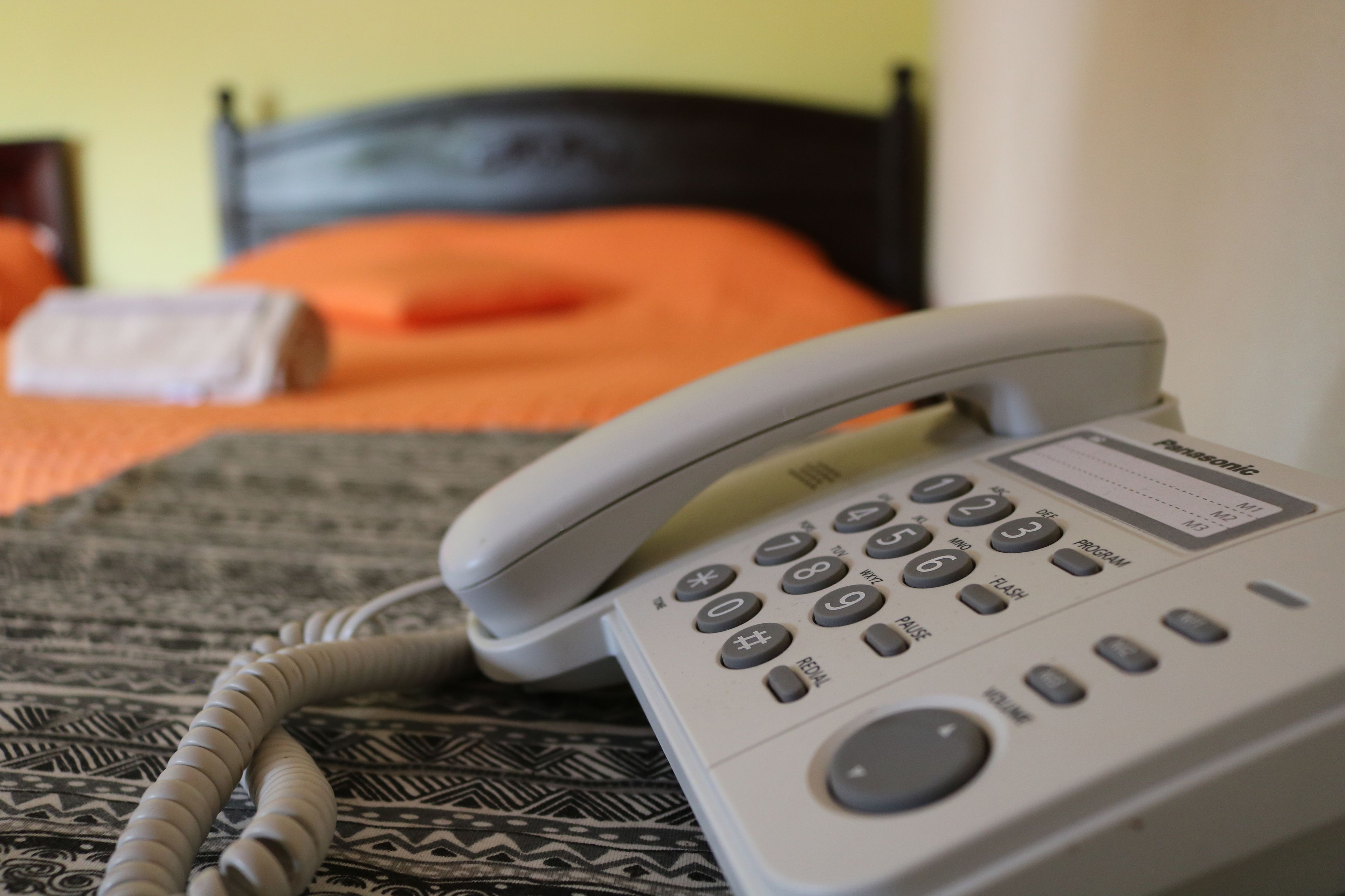 Un téléphone blanc est posé sur une couvre-lit à motifs dans une pièce dont la tête de lit est noire.