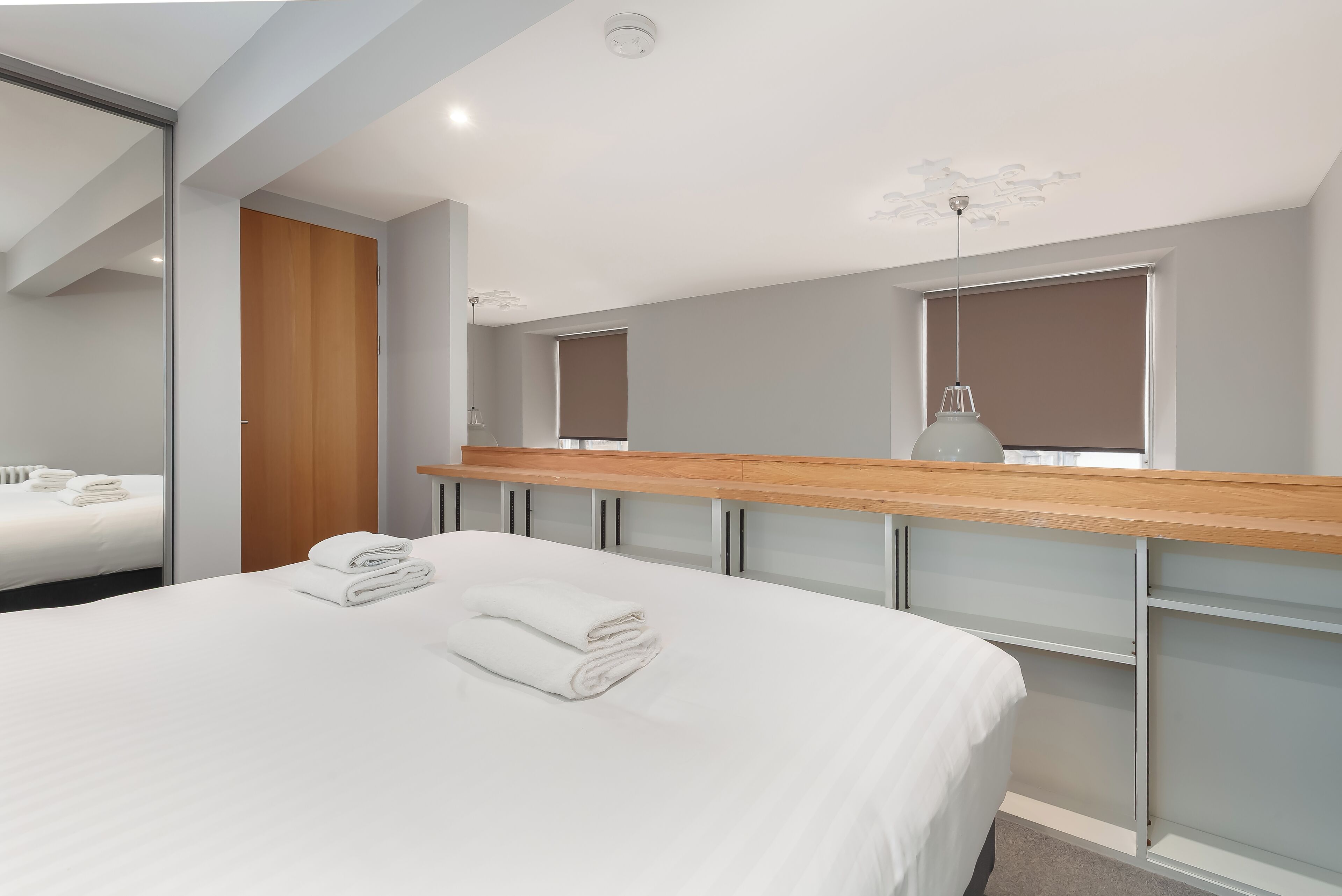 Habitación de hotel moderna con una cama grande, cabecera de madera, recinto de ducha de vidrio y un espejo amplio.