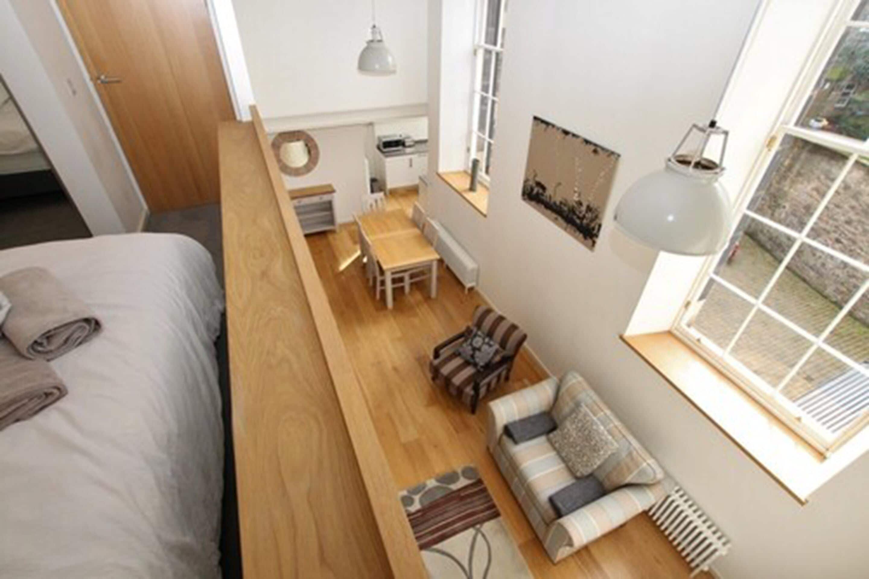 A compact room with a bed, a small dining table, a sofa, and a window providing natural light.