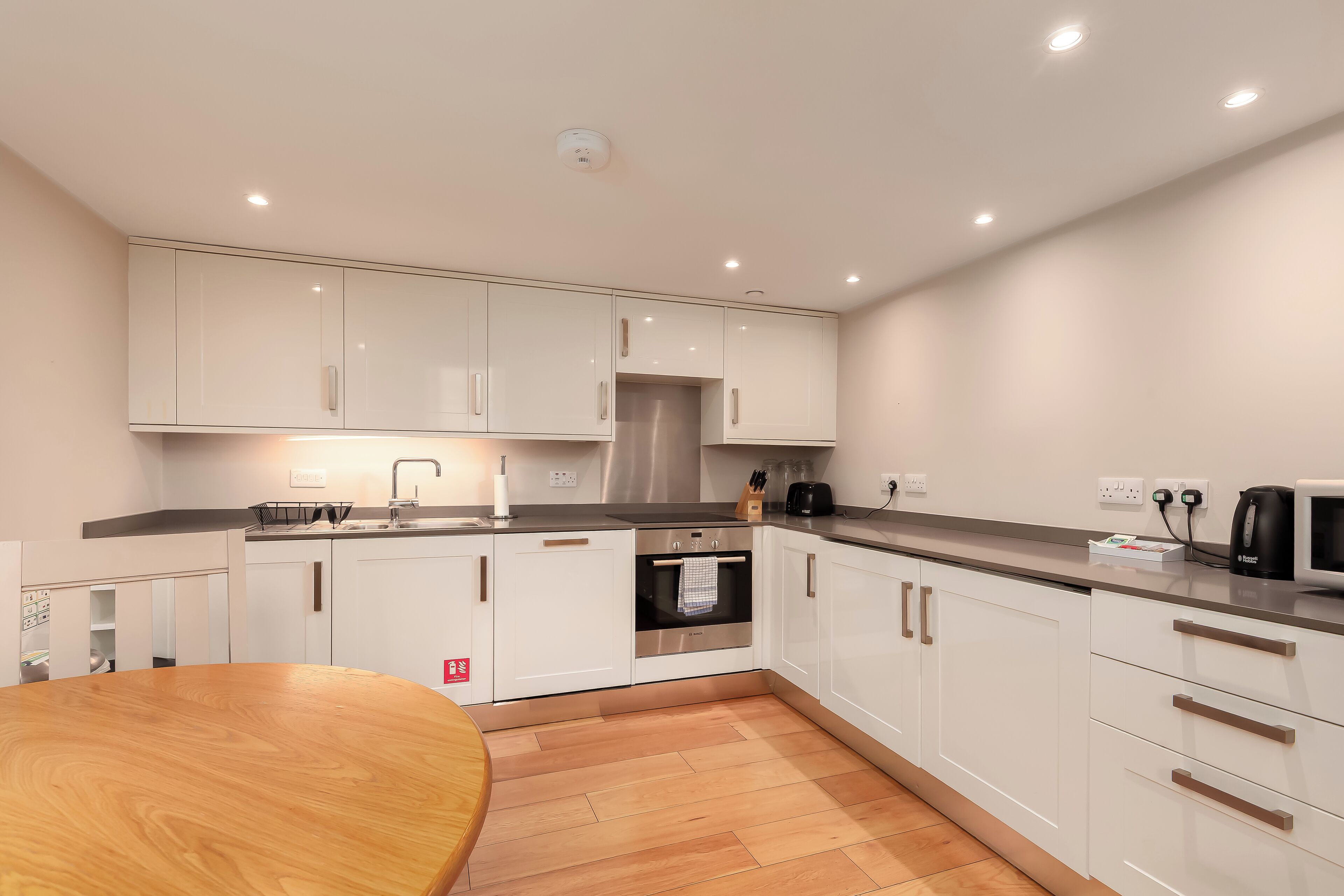 A modern kitchen with white cabinets, a stainless steel oven, and a wooden dining table.