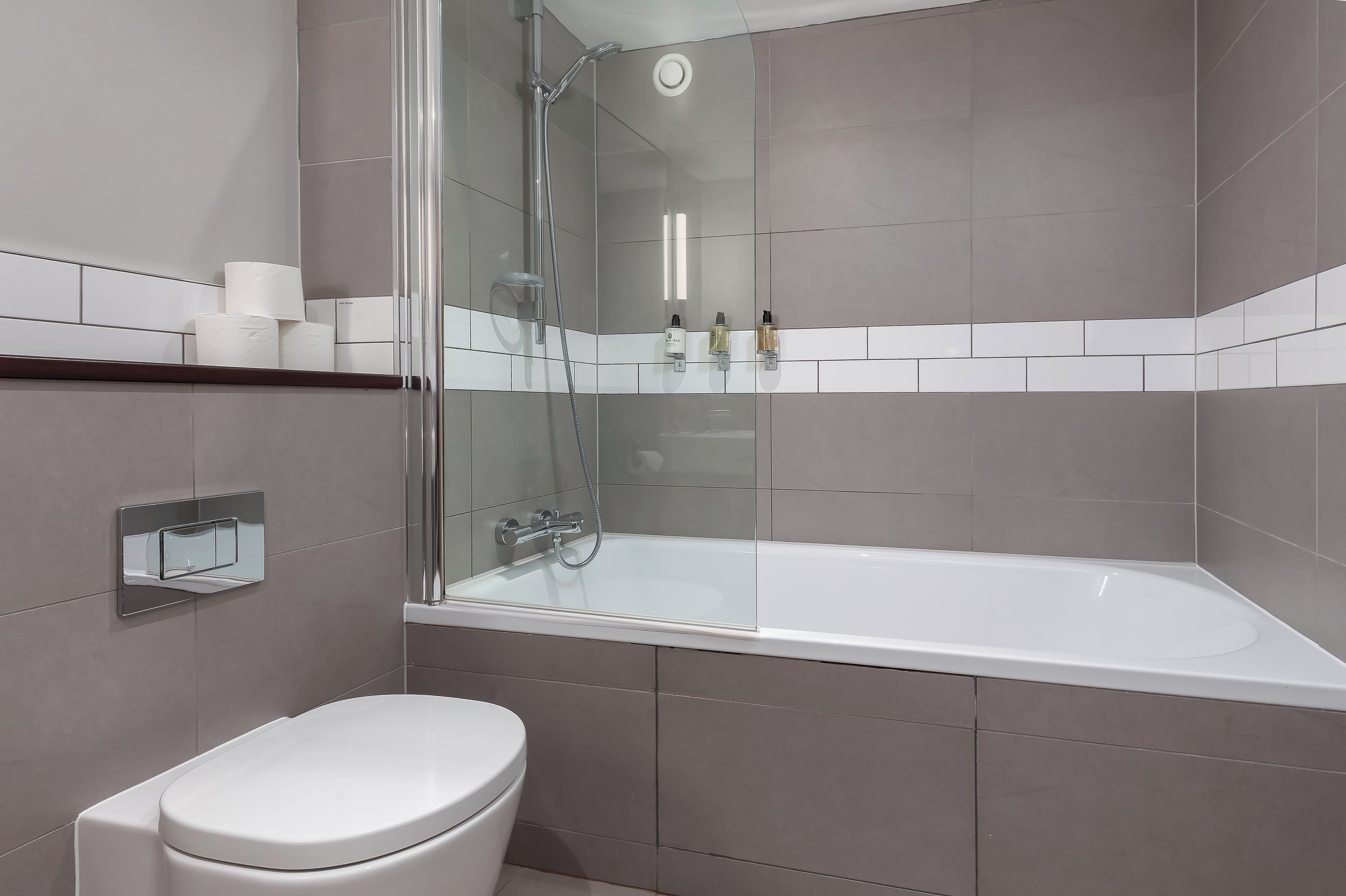 A modern bathroom with a glass-enclosed shower, a white bathtub, and a toilet.