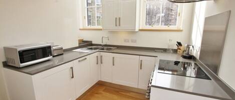 A modern kitchen with white cabinets, a microwave, a sink, and a stove.