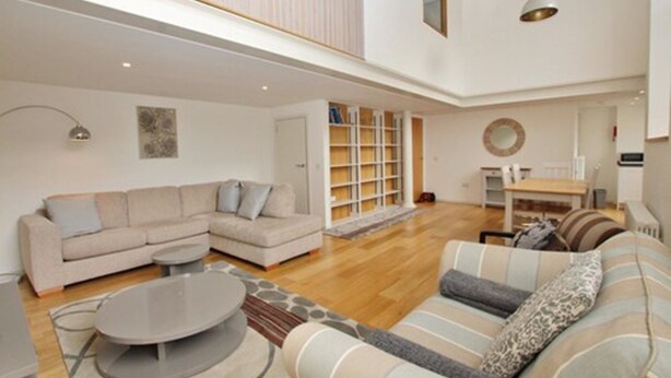 A spacious living area with a sectional sofa, a round coffee table, and a bookshelf. - Destiny Scotland - Broughton St Lofts (Edinburgh)