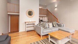 A modern living room with a grey sofa, wooden coffee table, and a staircase leading to an upper level. - Destiny Scotland - Broughton St Lofts (Edinburgh)