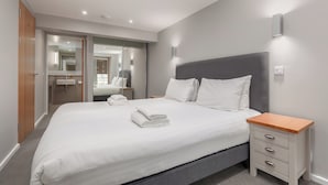 A modern hotel room with a large bed, a bedside table, a built-in wardrobe, and a bathroom with a mirror and sink. - Destiny Scotland - Broughton St Lofts (Edinburgh)
