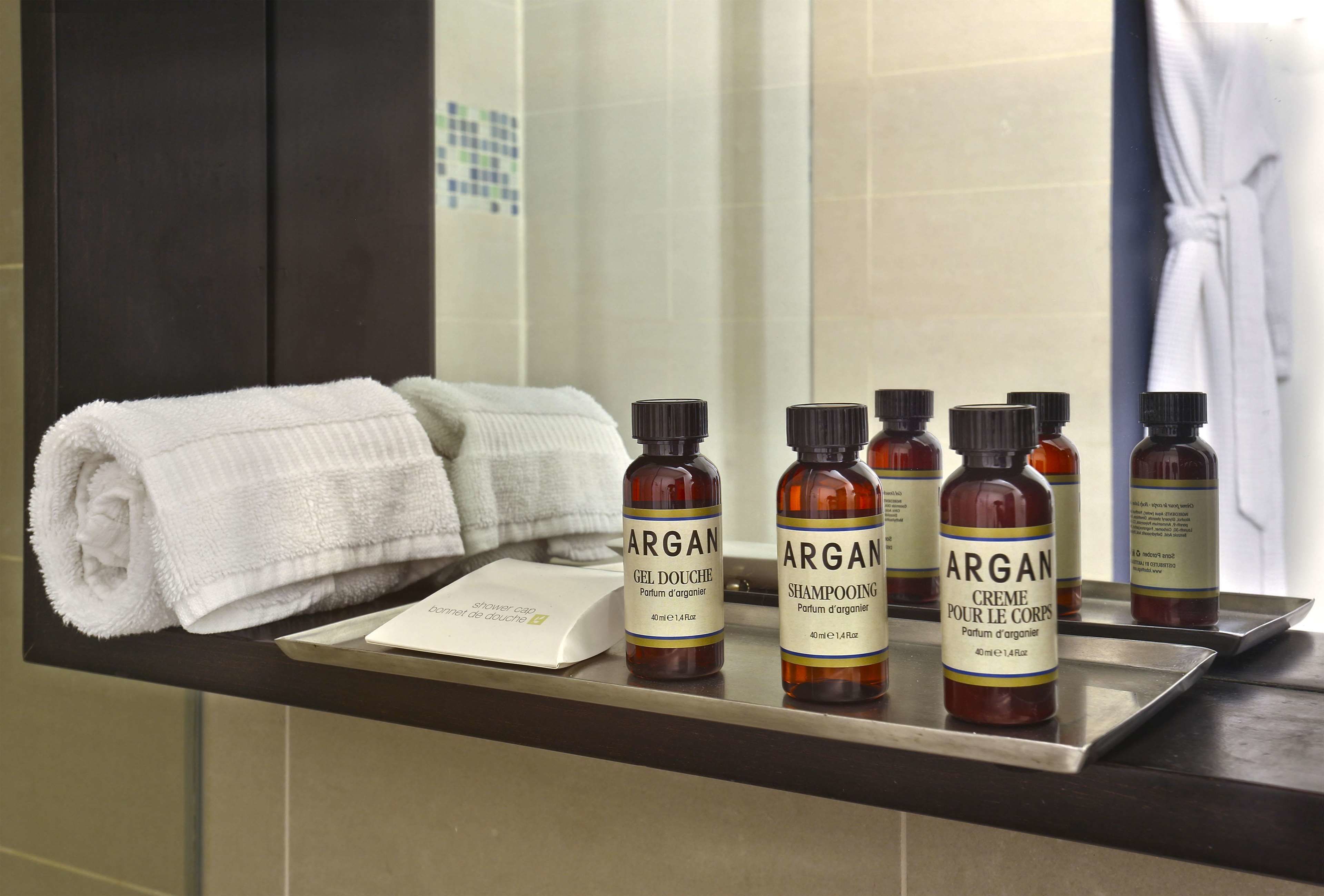 A bathroom with a towel rack holding a folded towel, and a shelf with four bottles of Argan products.
