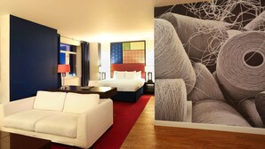 Hotellihuone, jossa on sänky, valkoinen sohva, työpöytä ja punainen matto.