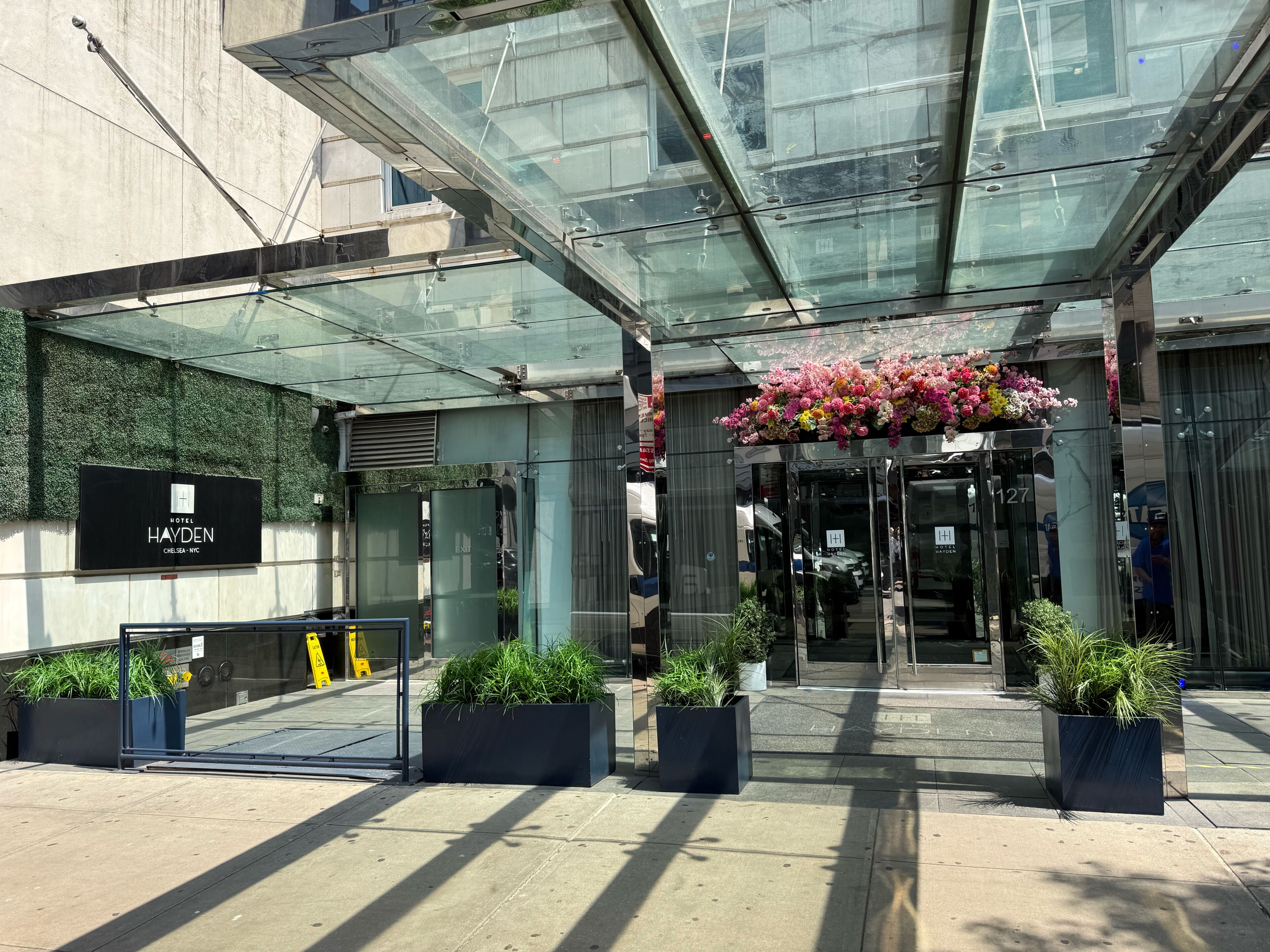 L’entrée d’un hôtel, avec un auvent en verre, une enseigne et des plantes en pot.