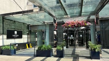 L’entrée d’un hôtel, avec un auvent en verre, une enseigne et des plantes en pot.