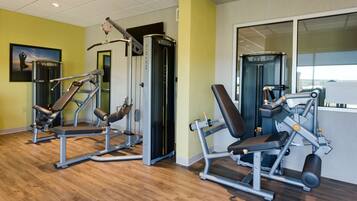 A gym with exercise equipment, wooden flooring, and a painting on the wall.