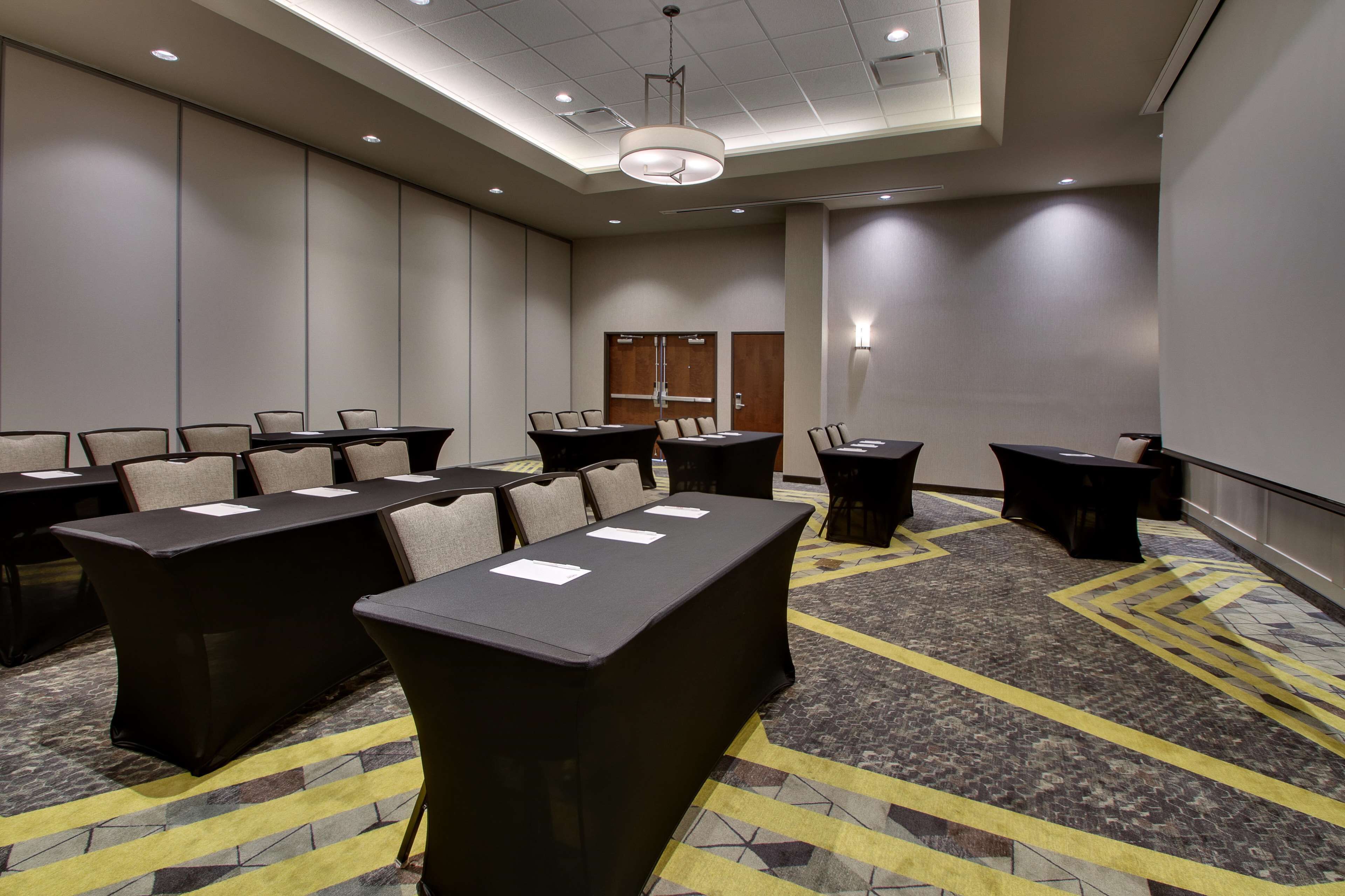 Une salle de conférence dotée de plusieurs tables et chaises, d’un tapis à motifs et d’un plafond équipé d’un éclairage encastré.