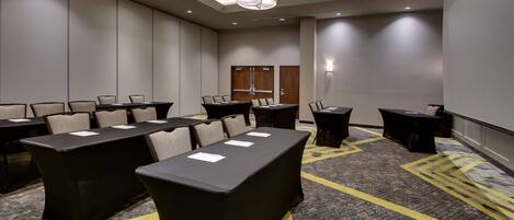 Une salle de conférence dotée de plusieurs tables et chaises, d’un tapis à motifs et d’un plafond équipé d’un éclairage encastré.