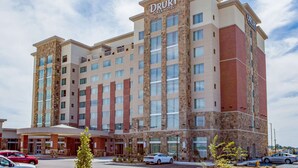 Un hotel Drury Plaza con un diseño moderno, que cuenta con una entrada destacada, varios pisos y un cielo despejado.