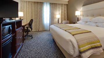 A hotel room with a large bed, a TV, a desk with a chair, and two lamps.