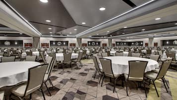 A large banquet hall with multiple round tables and chairs, equipped with ceiling lights and clocks on the walls.