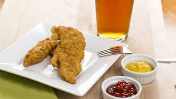 A plate of breaded and fried food items, two small bowls of condiments, and a glass of amber-colored liquid on a wooden table.