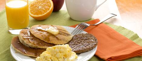 A breakfast plate with pancakes, sausage, scrambled eggs, and a glass of orange juice.