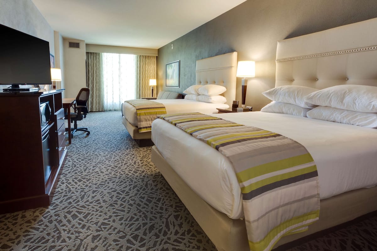 A hotel room with two beds, a desk, a television, and a chair.