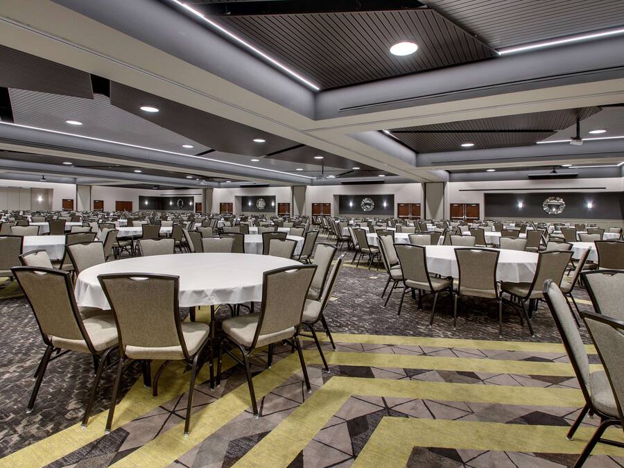 A large conference room with multiple round tables and chairs, arranged in rows.