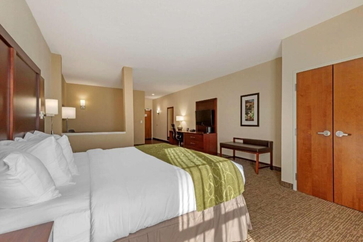 A hotel room with a bed, a desk, a chair, a wardrobe, and a mirror.